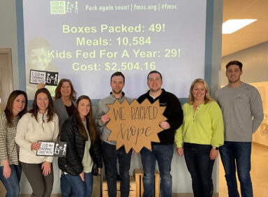 Employees in front of screen at Feed My Starving Children